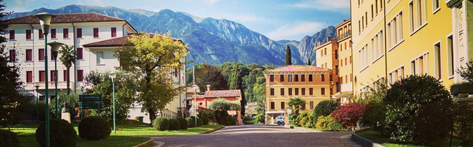A street with brightly colored buildings on both sides of the street. Tall mountains and trees are visible in the background. 